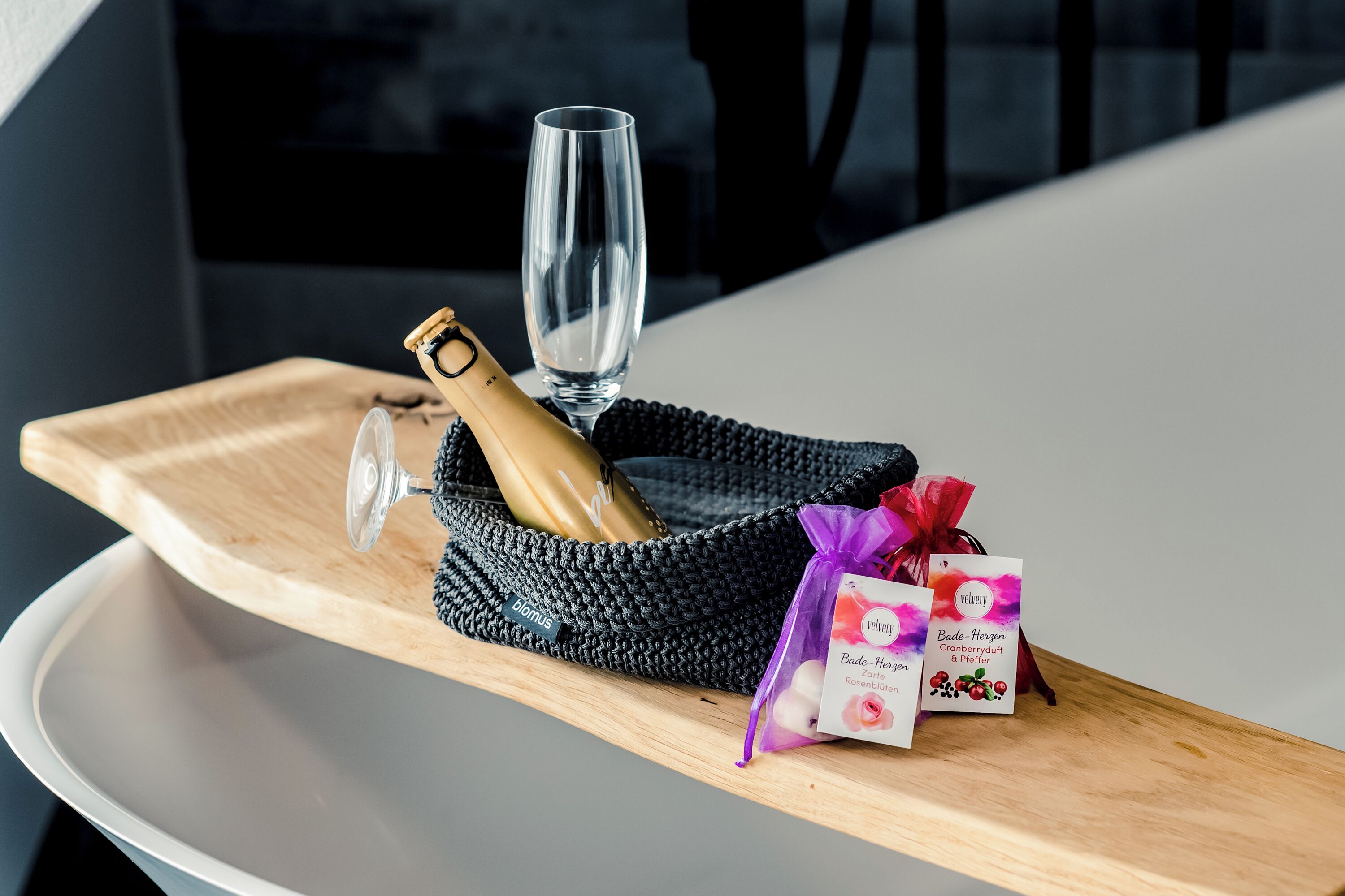 Ein Holztablett mit einer Champagnerflasche, einem Glas und zwei verpackten Gegenständen auf einem Tisch.