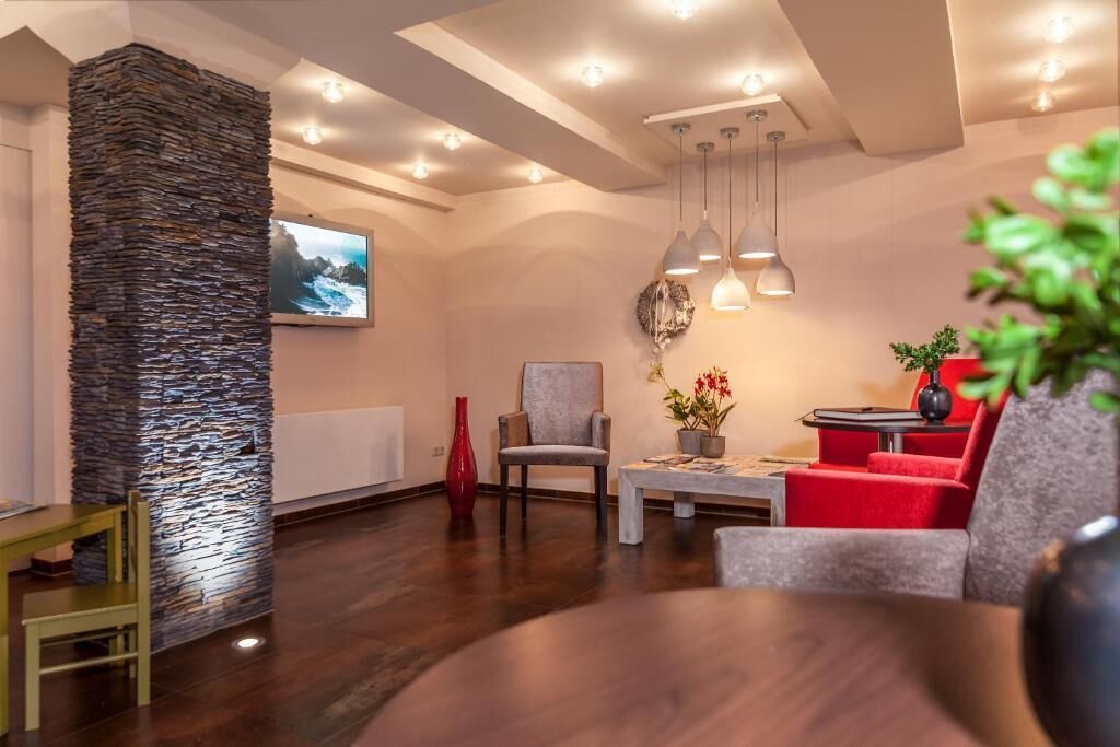 Una sala moderna con una pared de acento de piedra, un televisor y una zona de estar con sofás rojos y grises.