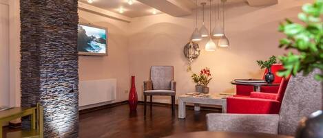 Una sala moderna con una pared de acento de piedra, un televisor y una zona de estar con sofás rojos y grises.