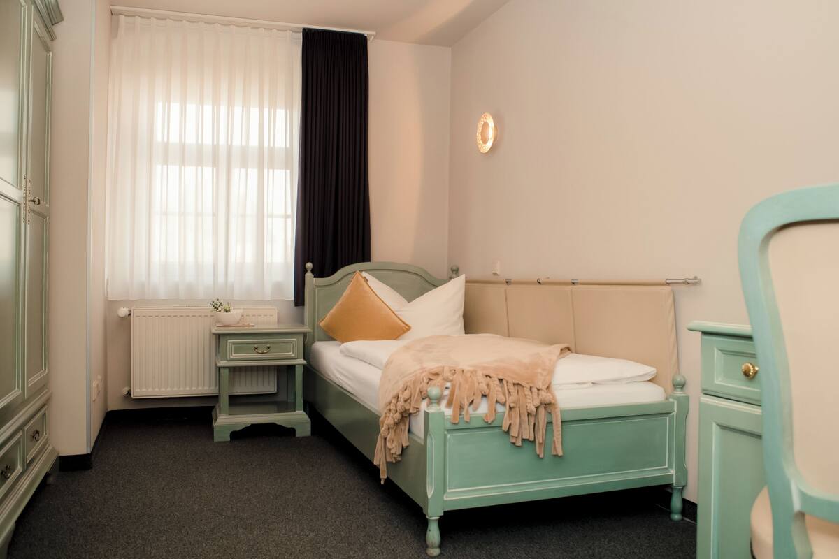 A room with a bed, a nightstand, a dresser, a window with curtains, and a wall clock.