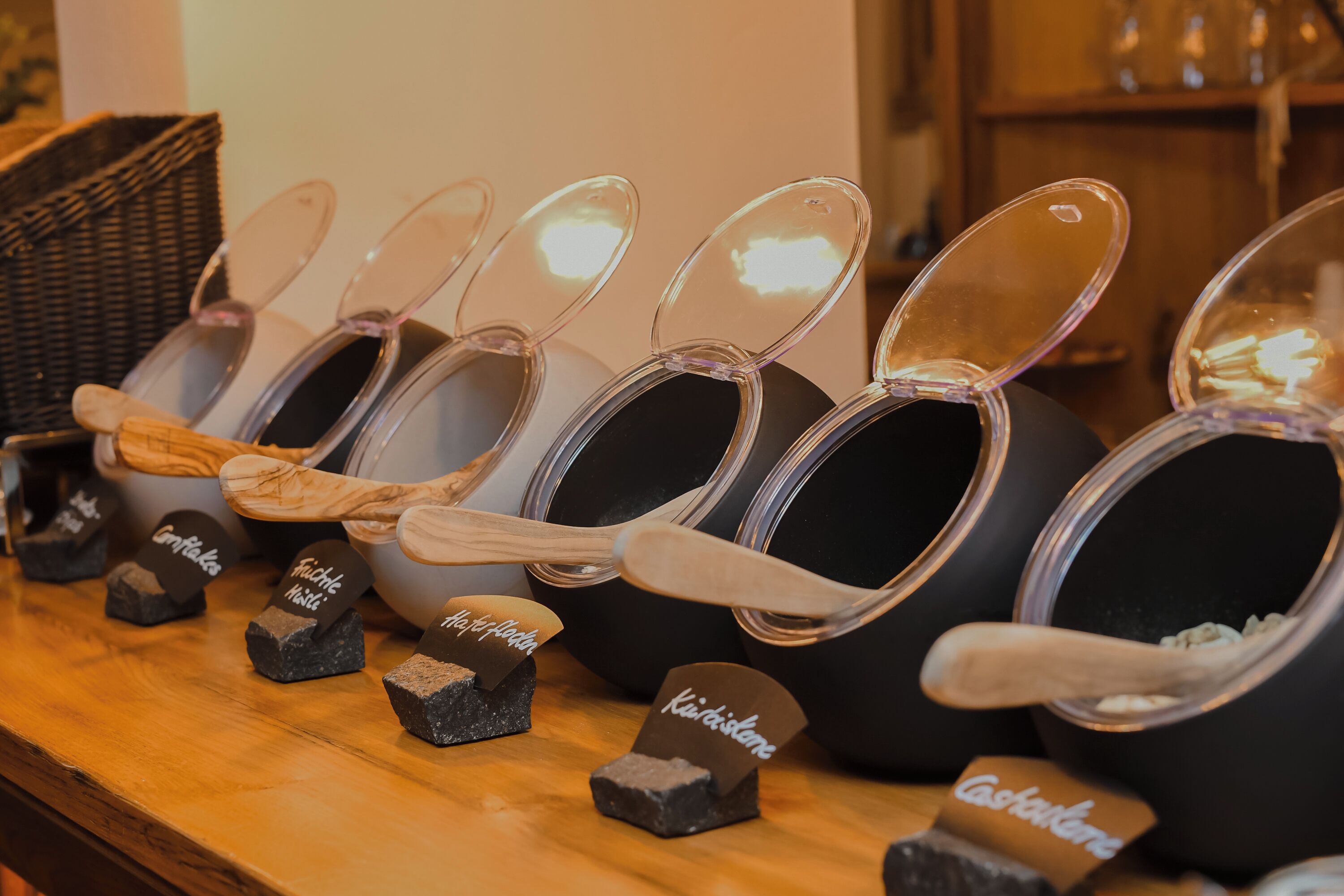 A row of black containers with clear lids, each labeled with a different type of chocolate.