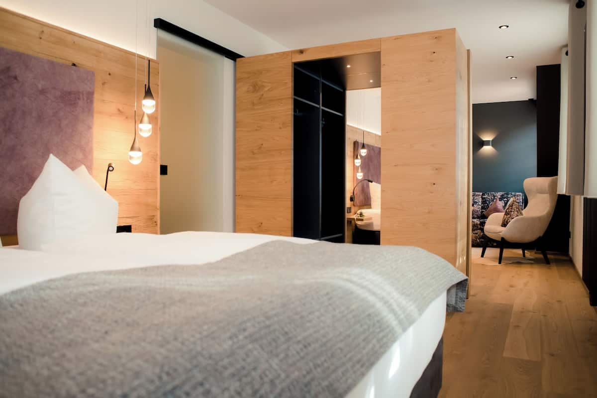 A modern hotel room with a large bed, wooden panel walls, and a seating area with a chair and table.