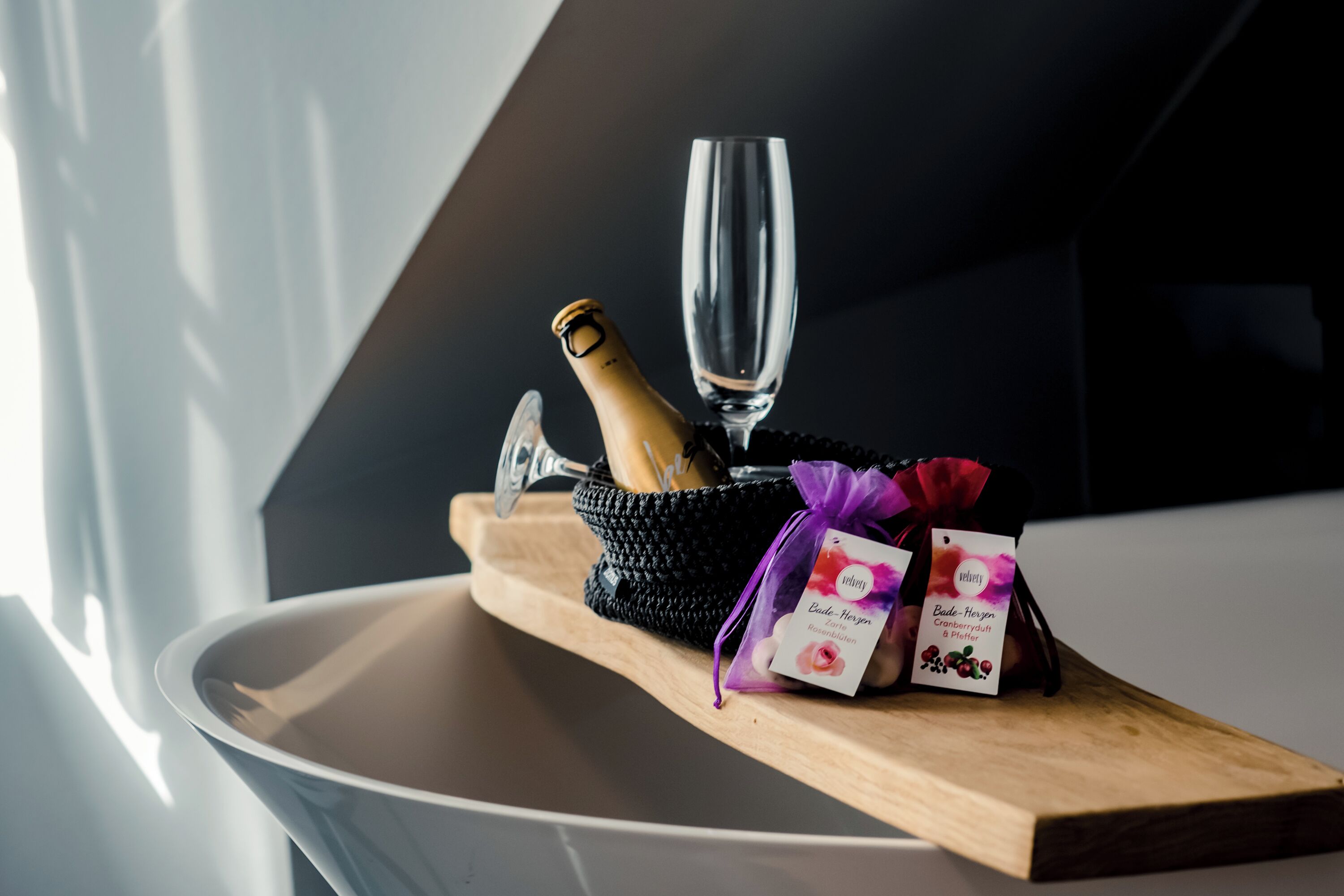 A bottle of champagne, a glass, and two gift bags on a wooden tray.