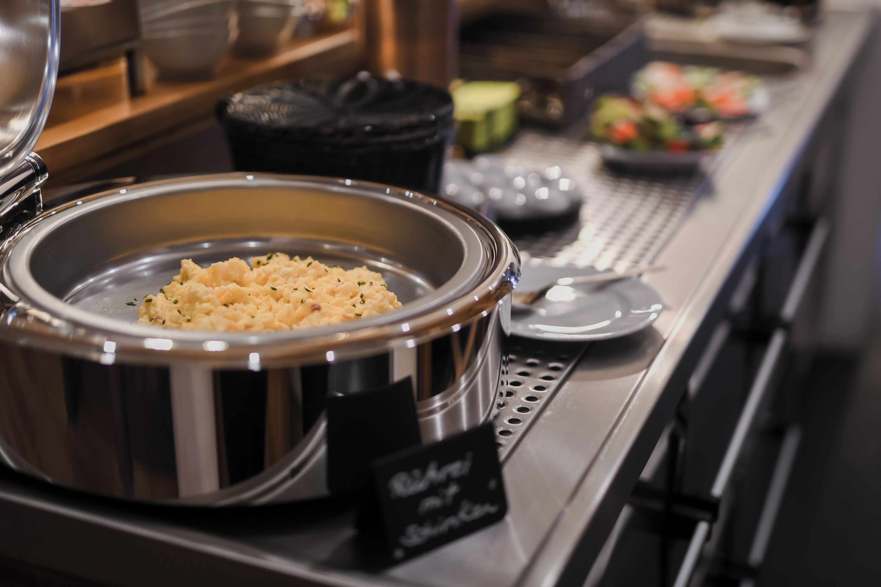 Un buffet avec un grand saladier en métal rempli de riz, une pancarte indiquant « Riz à la sauce vapeur », et divers autres plats en arrière-plan.