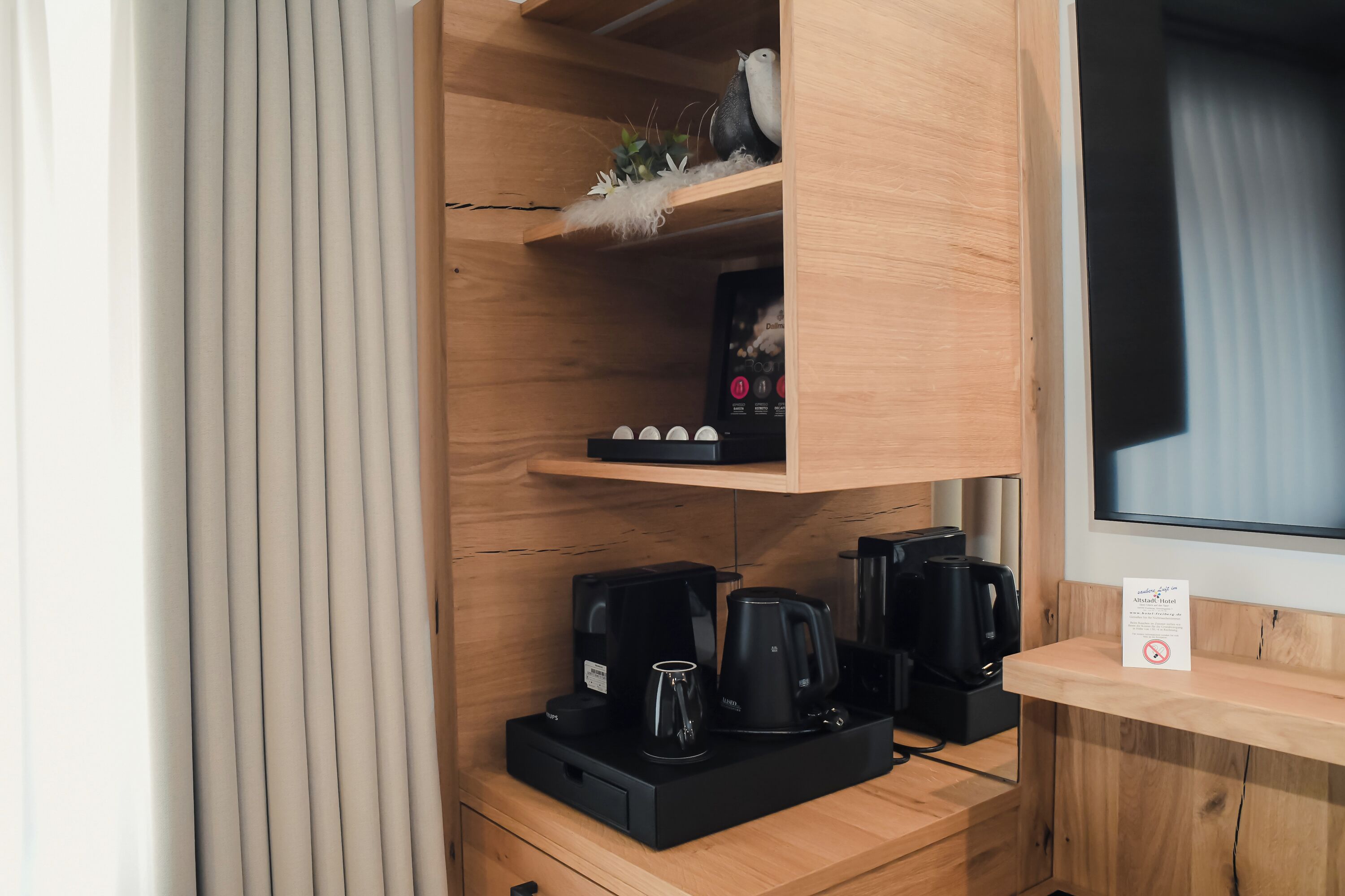 A compact kitchenette with a coffee maker, a kettle, and a mug on a wooden countertop.