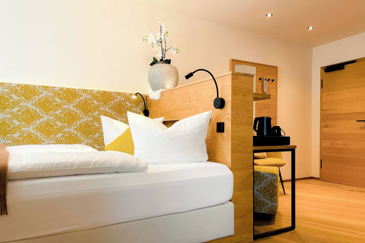 A modern bedroom with a white sofa, yellow patterned wallpaper, a small table with a coffee maker, and a wooden door.