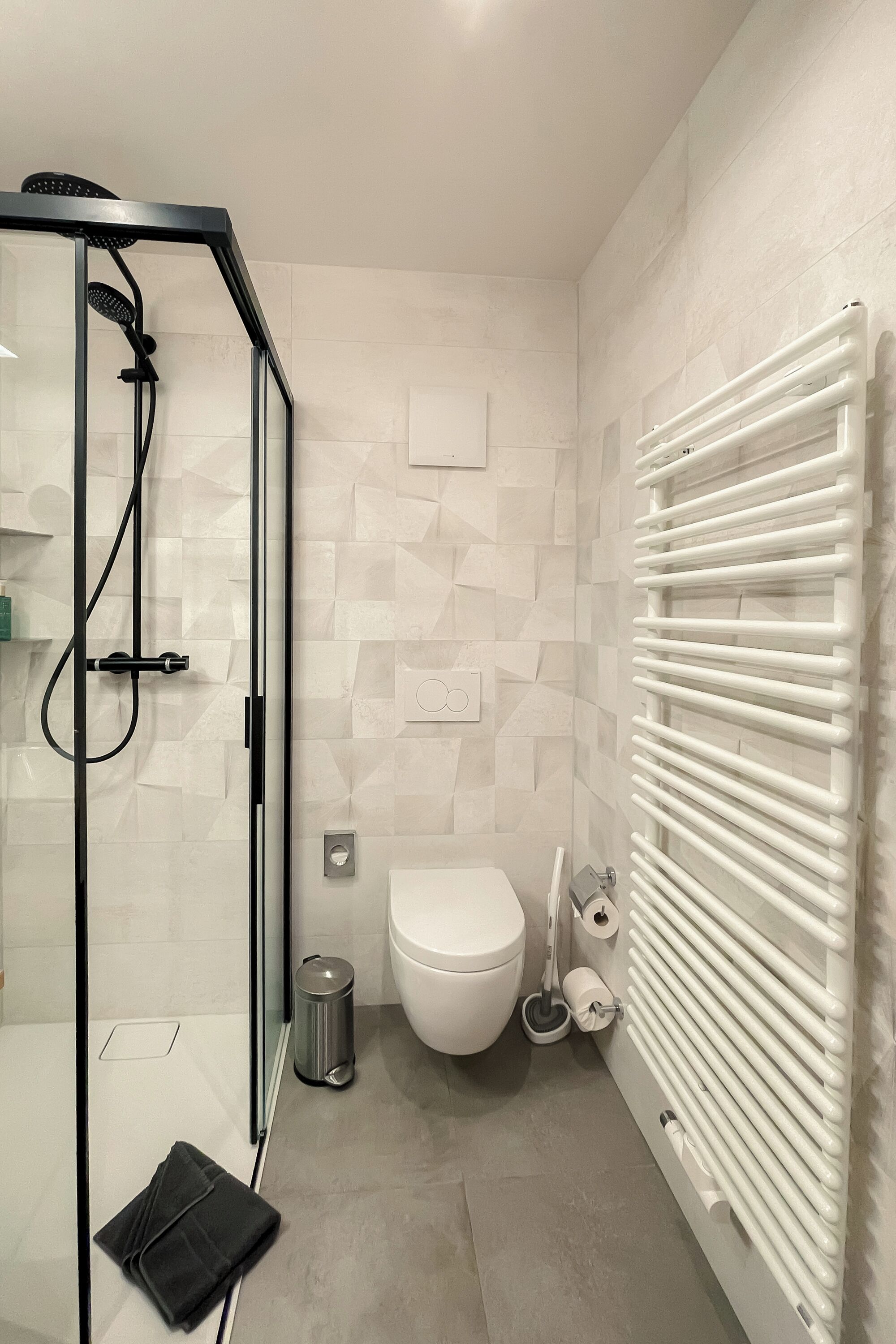 A modern bathroom with a glass shower enclosure, a white toilet, and a white radiator.