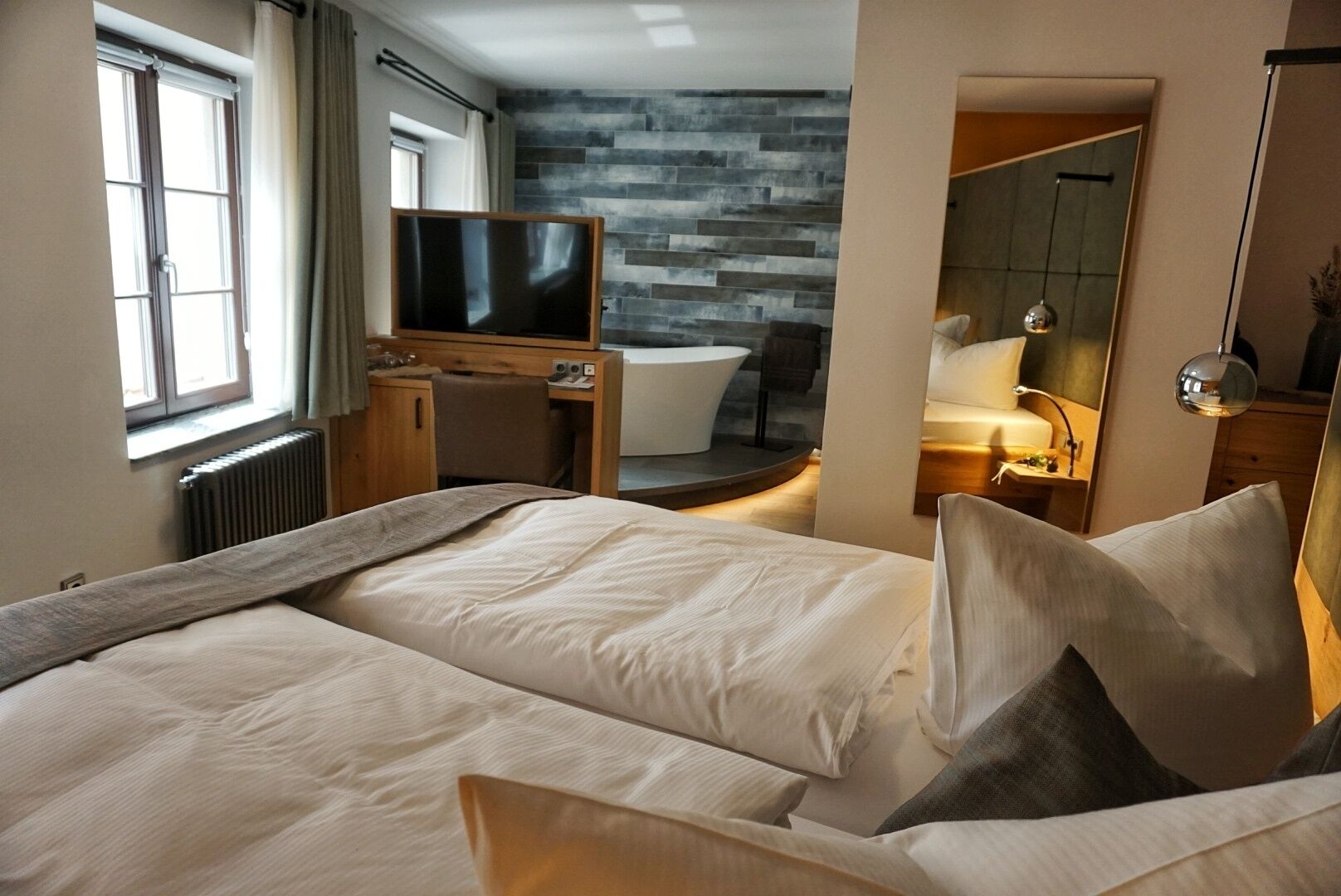 Een hotelkamer met een groot bed, een bureau met een stoel, een televisie, een badkamer met een badkuip, en een spiegel.