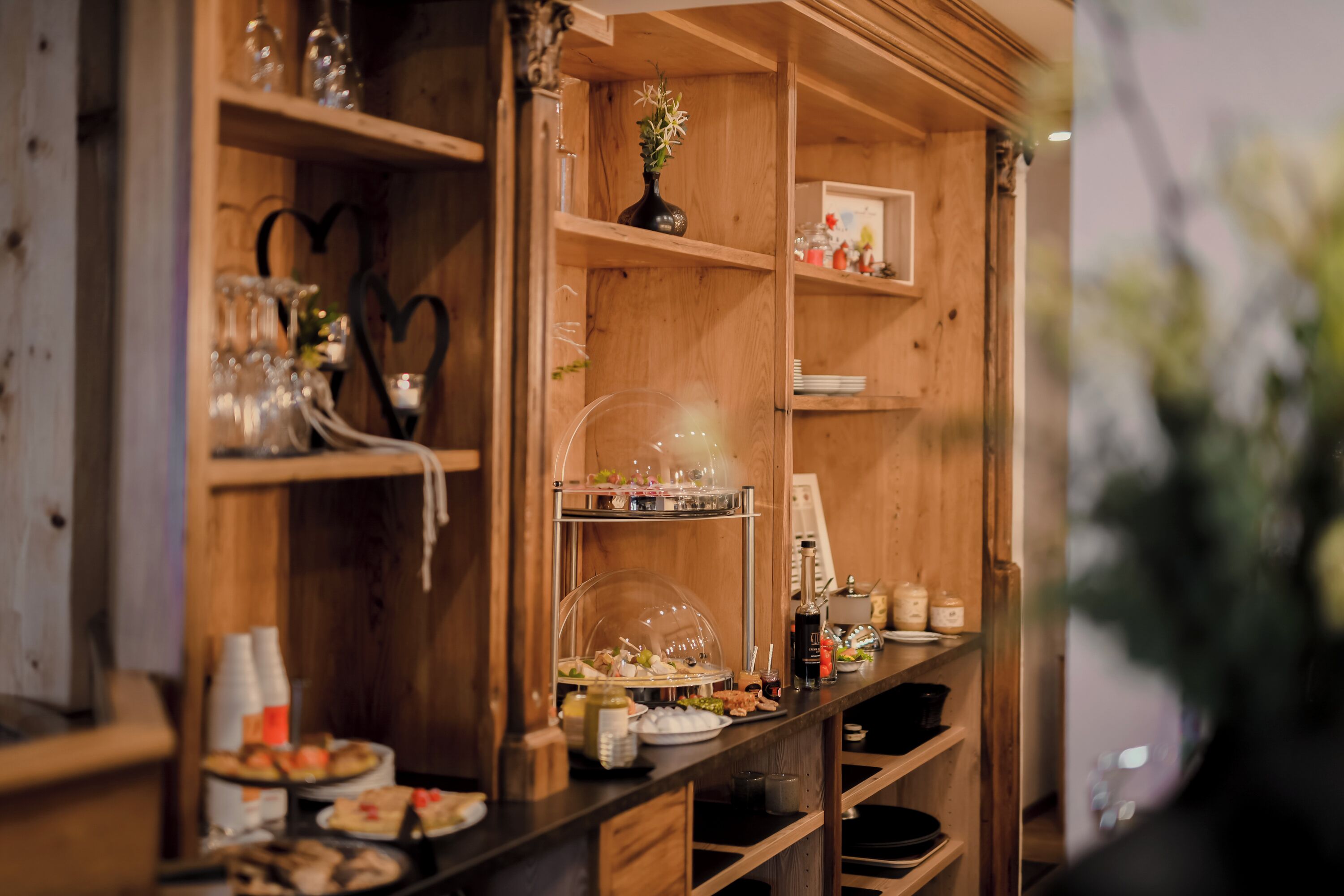 Un aparador de madera con cristalería, un jarrón con flores y diversos alimentos.