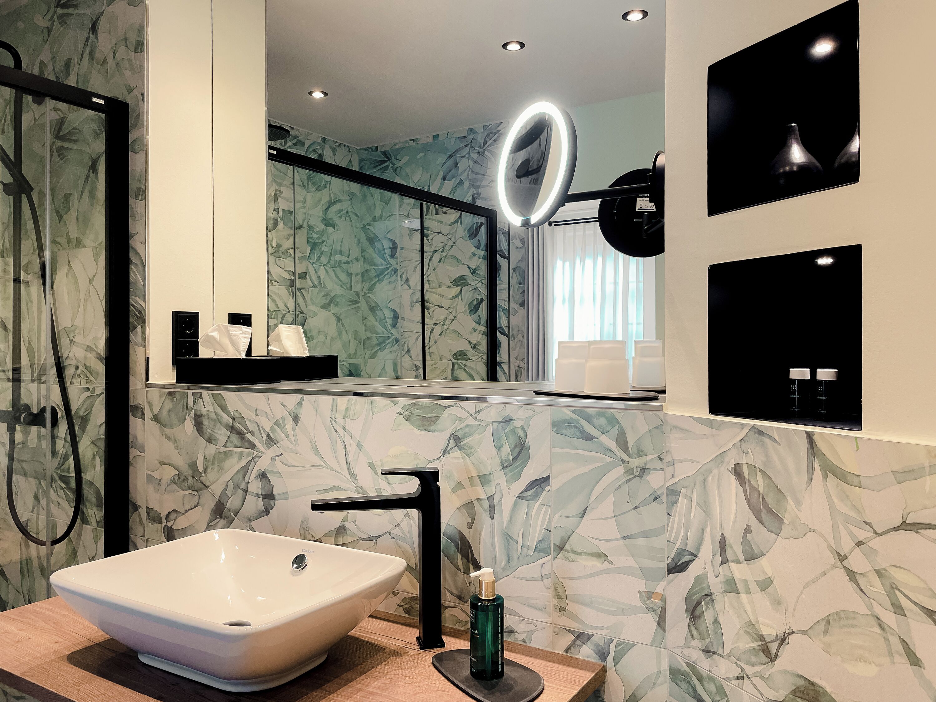 A bathroom with a large mirror, a white vessel sink, a black faucet, and a ring light.