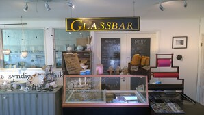 A glass bar with a chalkboard menu, various glassware, and a display case with glass items. - Elisetorp (Kivik)