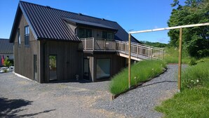 A two-story wooden house with a balcony, a gravel driveway, and surrounding greenery. - Elisetorp (Kivik)
