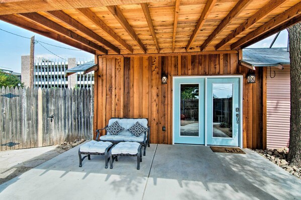 A covered patio with a wooden ceiling, a bench, and a door leading to a building.