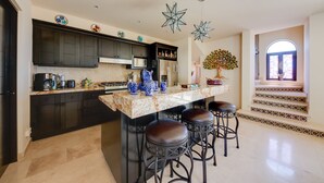 A modern kitchen with dark cabinets, a marble countertop, and a central island with stools. - ‘Casa Verde’ in Cabo San Lucas -  3 Mi to Marina! (Cabo San Lucas)