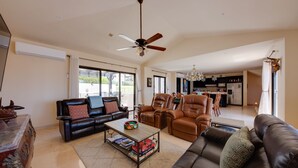 A spacious living room with a black leather sofa, a brown leather armchair, and a coffee table with books. There is a ceiling fan and a chandelier. - ‘Casa Verde’ in Cabo San Lucas -  3 Mi to Marina! (Cabo San Lucas)