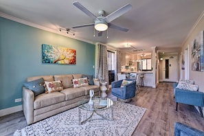 A living room with a beige sofa, a glass coffee table, and a ceiling fan. - Walk to Beach: West Maui Condo w/ Lanai & Pool! (Lahaina)