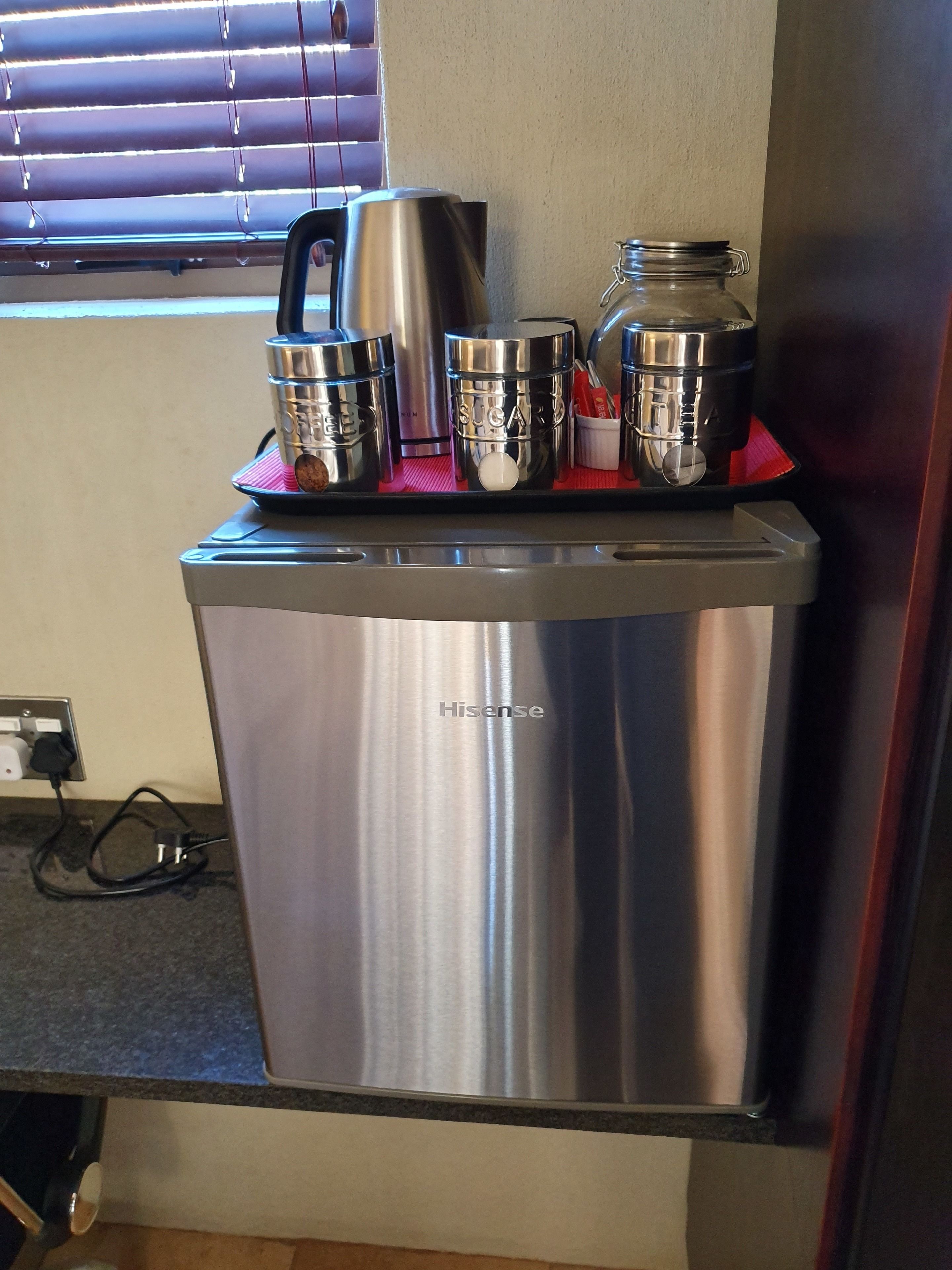 A stainless steel Hisense refrigerator with a built-in coffee maker, a jar of sugar, and a container of coffee pods.