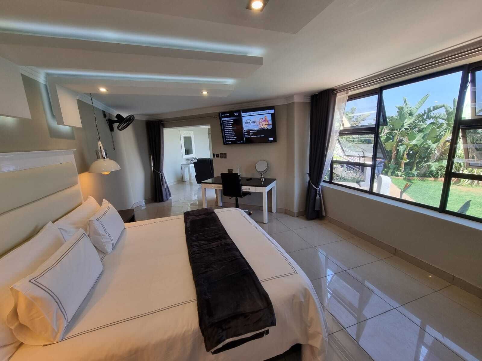 A modern hotel room with a large bed, a desk, a TV, and a view of the outdoors.