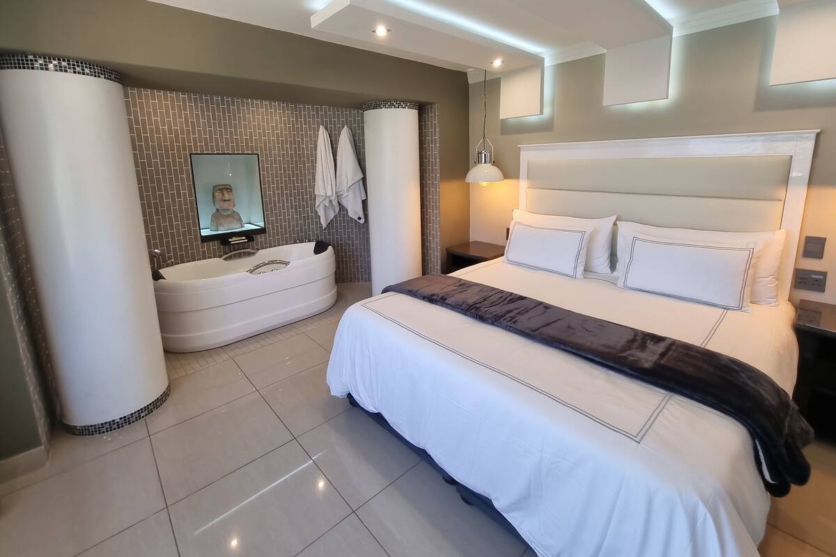 Een moderne slaapkamer met een groot bed, een inbouwbubbelbad en een wastafel met spiegel.