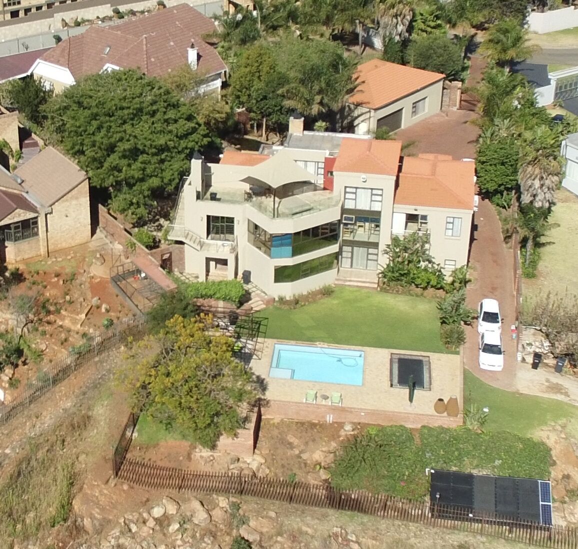 A modern two-story house with a swimming pool, surrounded by a fenced yard and neighboring houses.