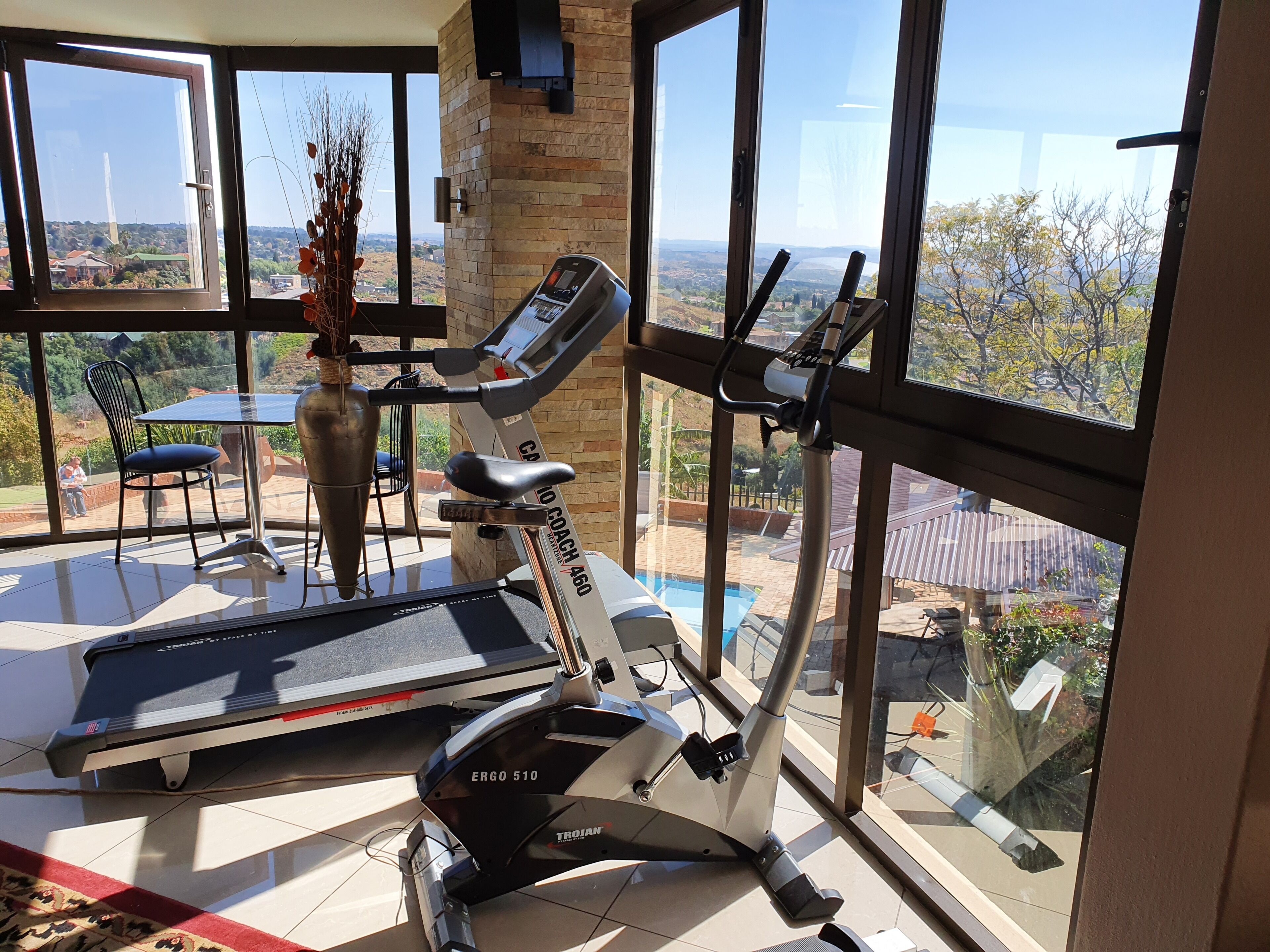 Un gimnasio en casa con cinta de correr y máquina elíptica, ventanas amplias que ofrecen vista a una zona residencial.