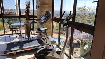 Un gimnasio en casa con cinta de correr y máquina elíptica, ventanas amplias que ofrecen vista a una zona residencial.