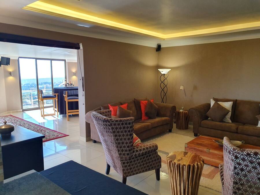 A modern living room with a sofa, armchair, and coffee table. There is a dining area with a table and chairs visible through a glass door.
