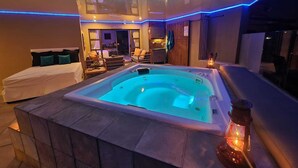 Een wellnessruimte met een bubbelbad, een zithoek en uitzicht op het buitengebeuren.
