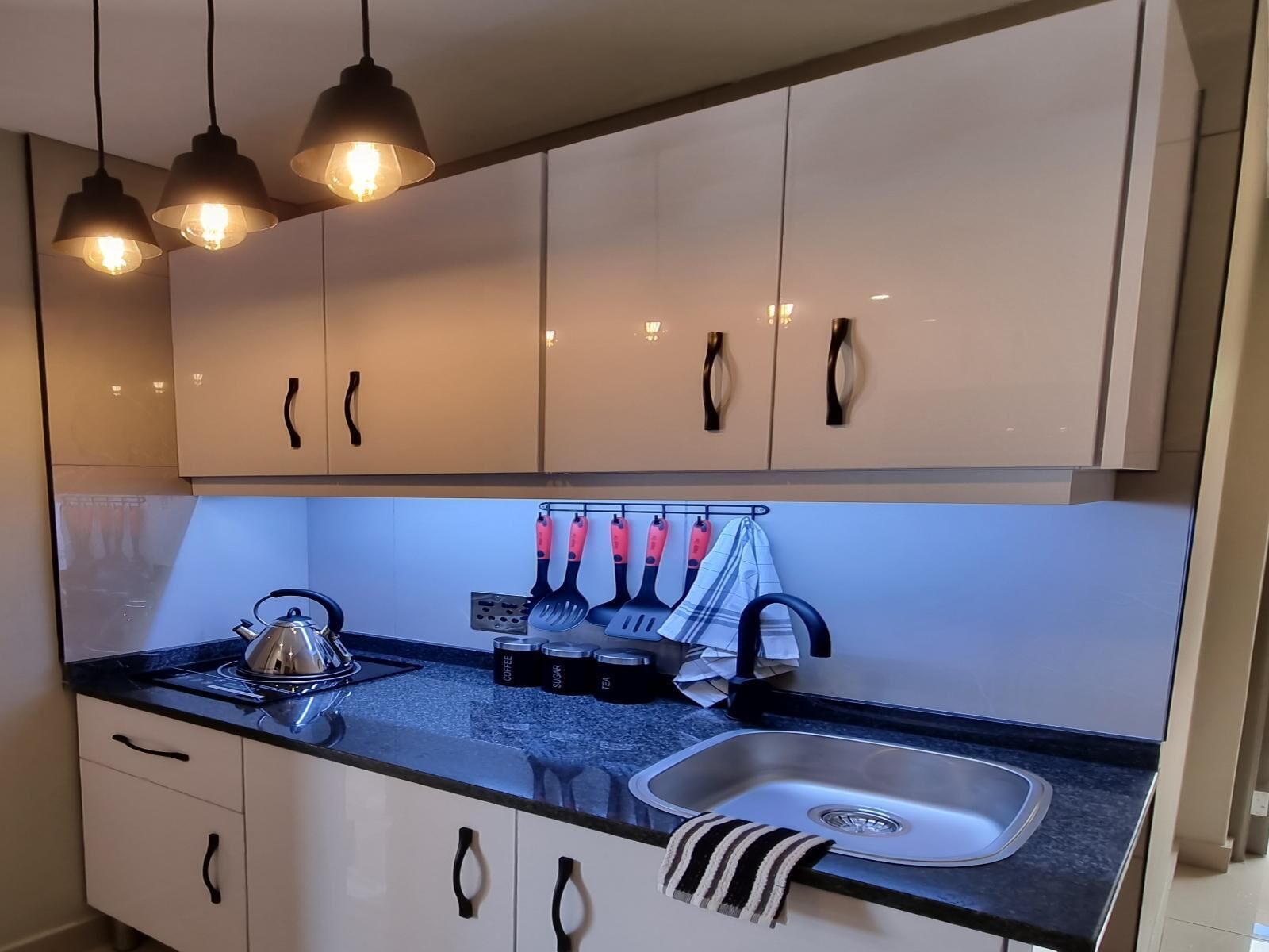 Una cocina moderna con armarios blancos, una encimera negra, una tetera, una cafetera y un fregadero.