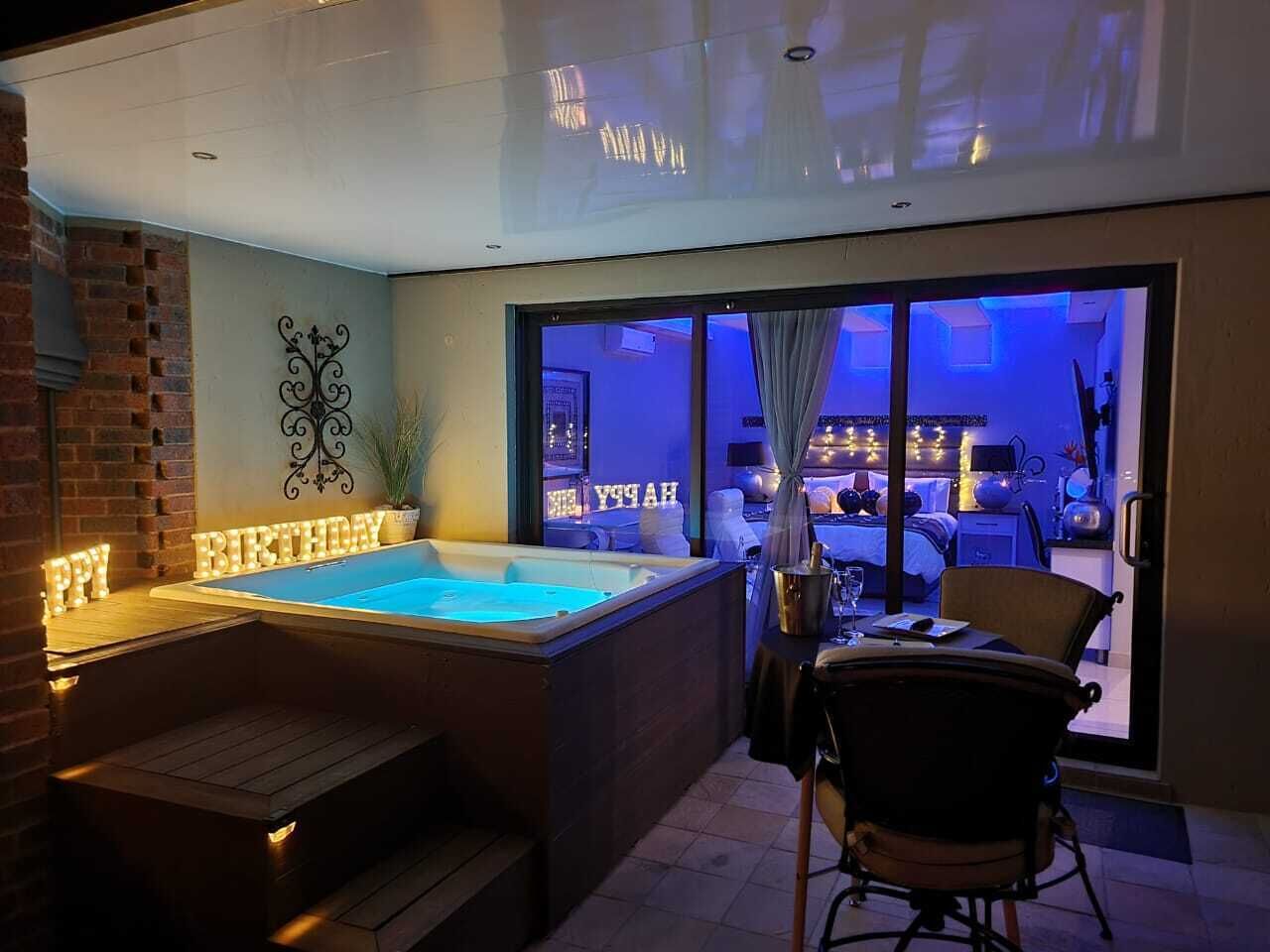 Zona de hidromasaje con banco de madera, una mesa con sillas y vista a un dormitorio a través de una puerta de cristal.