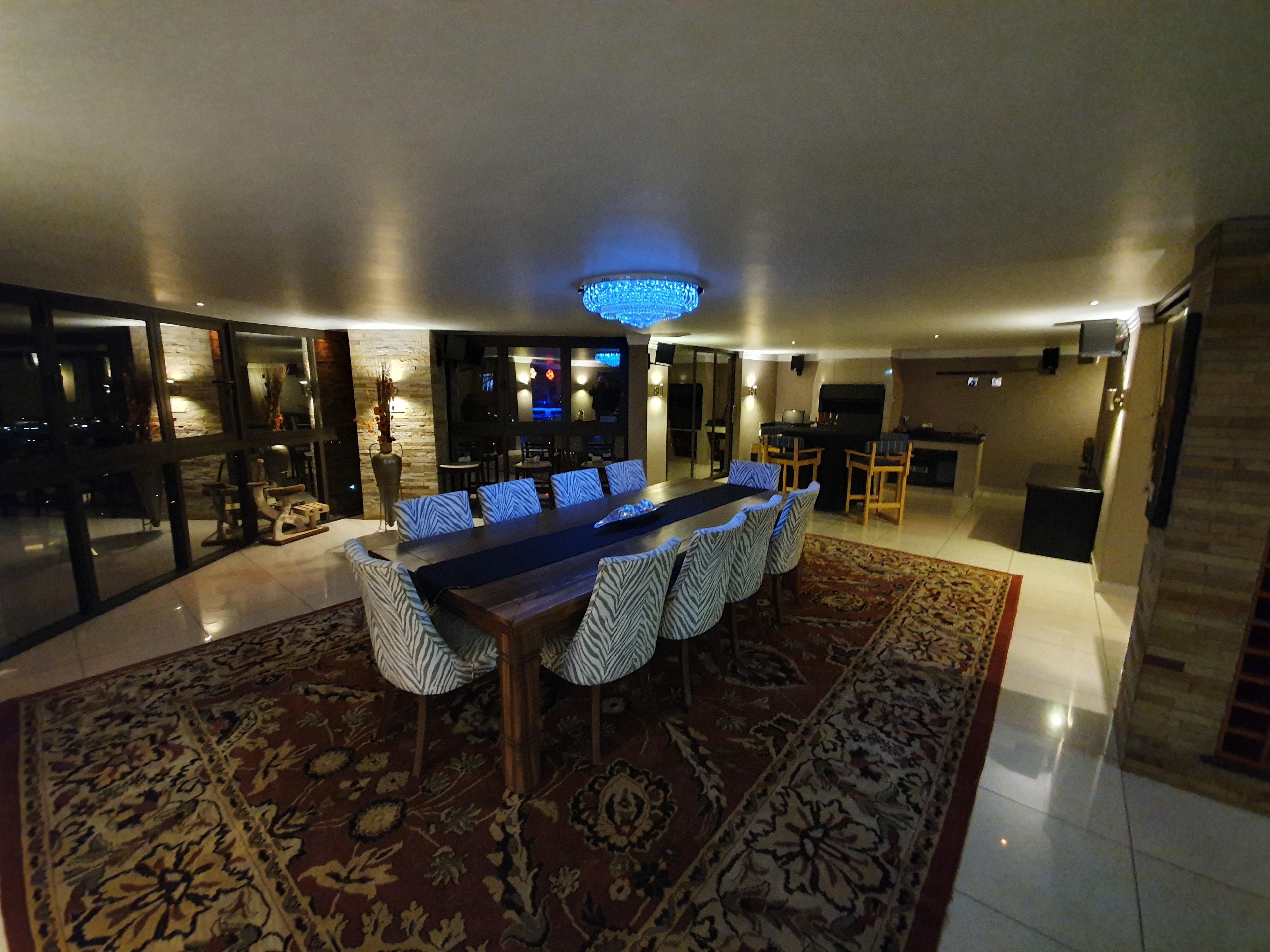 Un espace de salle à manger moderne, avec une longue table, des chaises à motifs et un tapis décoratif.