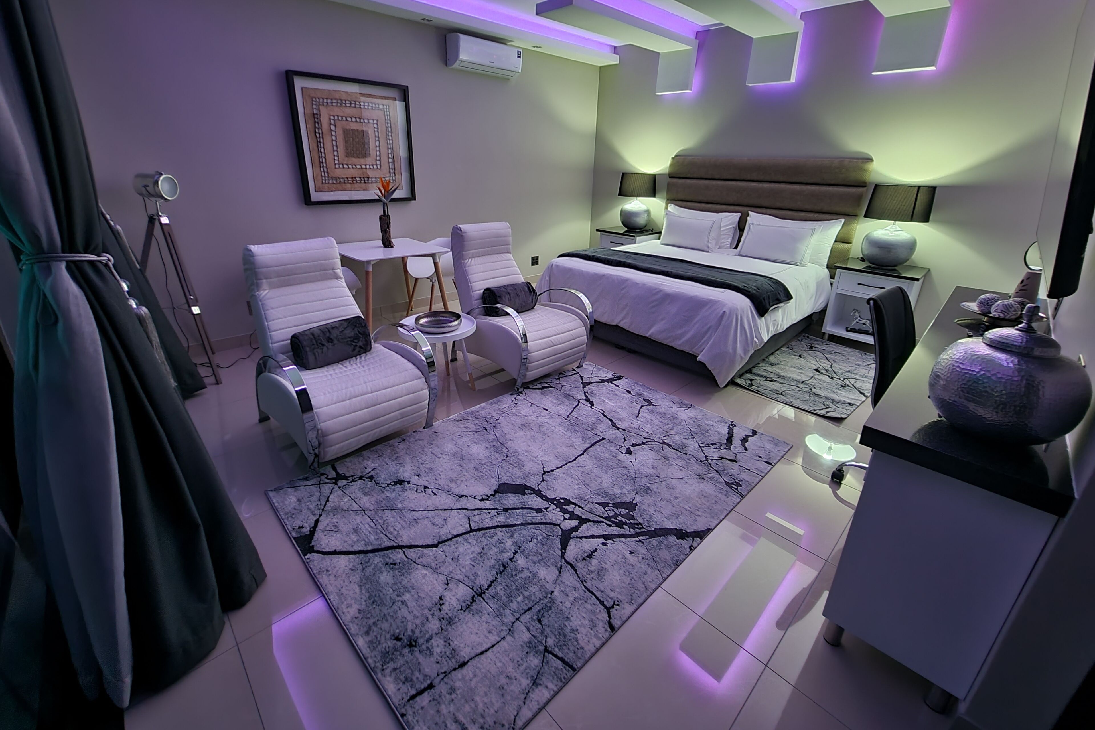 A modern hotel room with a bed, two chairs, a desk, and a large rug.