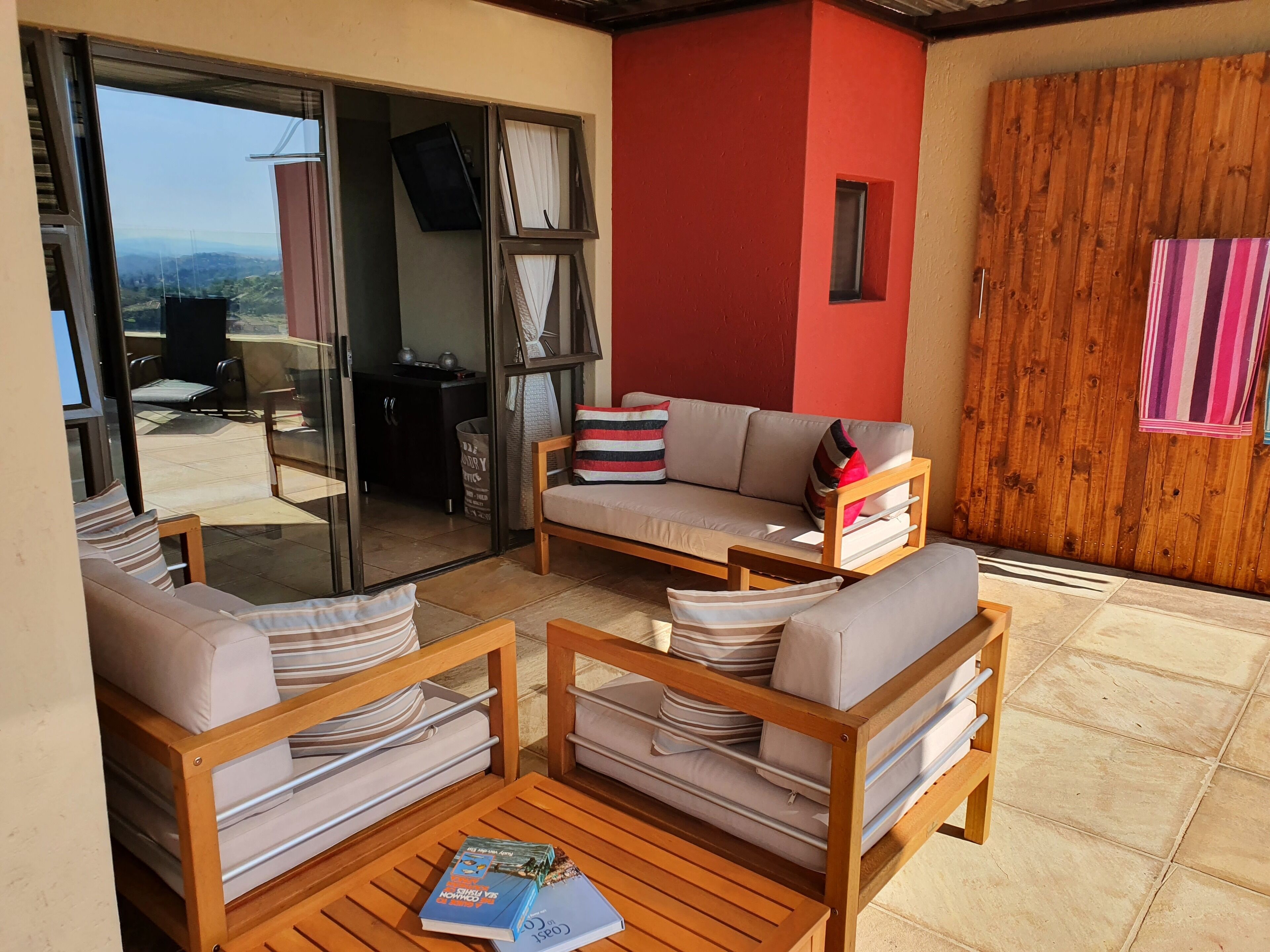 A cozy outdoor seating area with a sofa and chairs, a wooden table, and a view through a glass door.