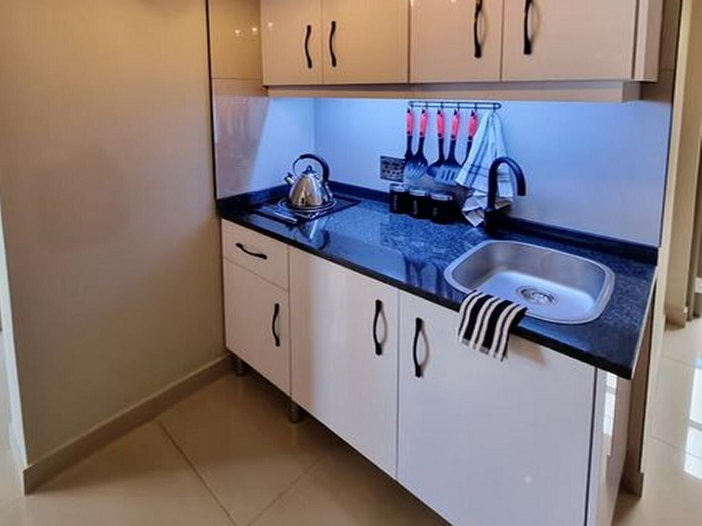 Una cocina compacta con un lavamanos, una tetera y un portalapices.