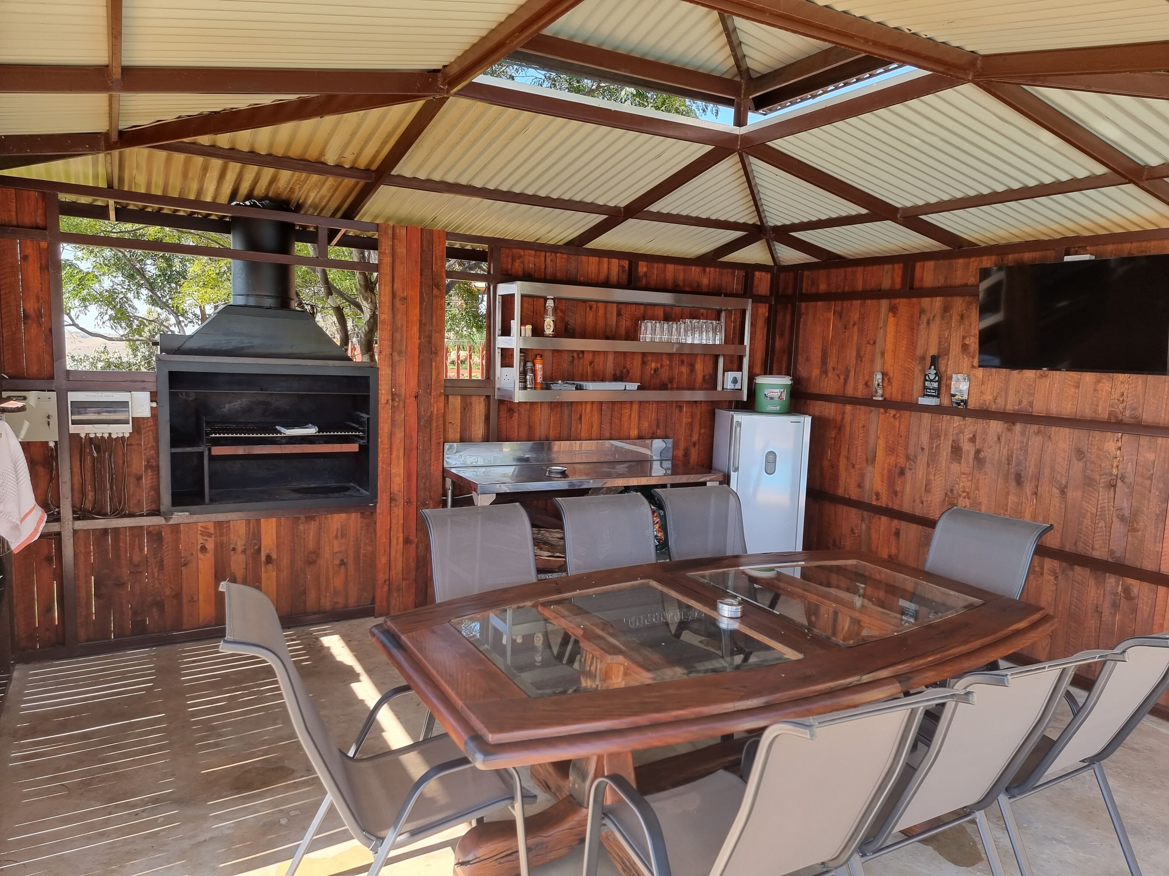 A covered outdoor dining area with a grill, seating, and a refrigerator.
