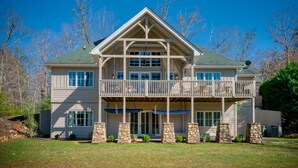 A two-story house with a balcony, stone pillars, and a green roof. - Elegant Mountain Dream Escape: 3BR with Fireplace & Views (Mill Spring)