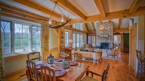 A spacious dining area with wooden furniture, a stone fireplace, and large windows. - Elegant Mountain Dream Escape: 3BR with Fireplace & Views (Mill Spring)