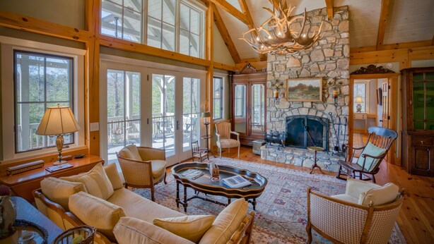 A spacious living room with a stone fireplace, large windows, and wooden beams. - Elegant Mountain Dream Escape: 3BR with Fireplace & Views (Mill Spring)