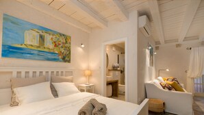 Une chambre d’hôtel avec un lit, un canapé, un tableau accroché au mur et une salle de bain visible à travers une porte ouverte.