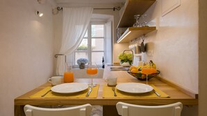 Une table de petit-déjeuner dressée avec des assiettes, des couverts et un panier de fruits.