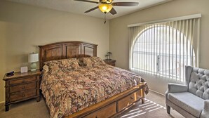 Un dormitorio con una cama grande, un ventilador de techo, una ventana con persianas, una mesita de noche y una silla.
