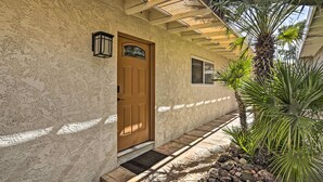 Fachada de estuco con una puerta de madera, una ventana pequeña y una palmera.