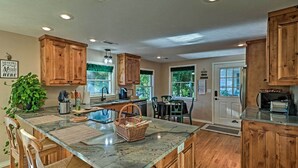 A kitchen with wooden cabinets, a marble countertop, and a dining area with chairs and a table. - 'Riverside Hide-A-Way' w/ Fire Pit, Fishing, BBQ (Mountain Home)