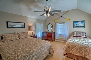 Une chambre avec un grand lit, un lit plus petit, un ventilateur de plafond, une commode, un miroir et deux fenêtres avec des rideaux.