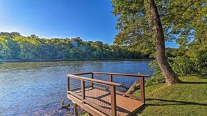 A wooden deck with a metal railing overlooking a lake, surrounded by trees and grassy areas. - 'Riverside Hide-A-Way' w/ Fire Pit, Fishing, BBQ (Mountain Home)