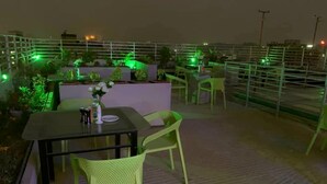 An outdoor terrace with a table and chairs, surrounded by greenery and illuminated by green lights. - The Alina Hotel & Suites (Chittagong)