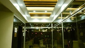 A modern interior with a glass partition, wooden ceiling beams, and recessed lighting. - The Alina Hotel & Suites (Chittagong)
