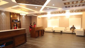 A hotel reception area with a wooden reception desk, two receptionists, and a waiting area with sofas and a coffee table. - The Alina Hotel & Suites (Chittagong)