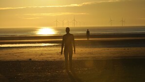A beach with people walking, and wind turbines in the distance. - Aberley House (Liverpool)