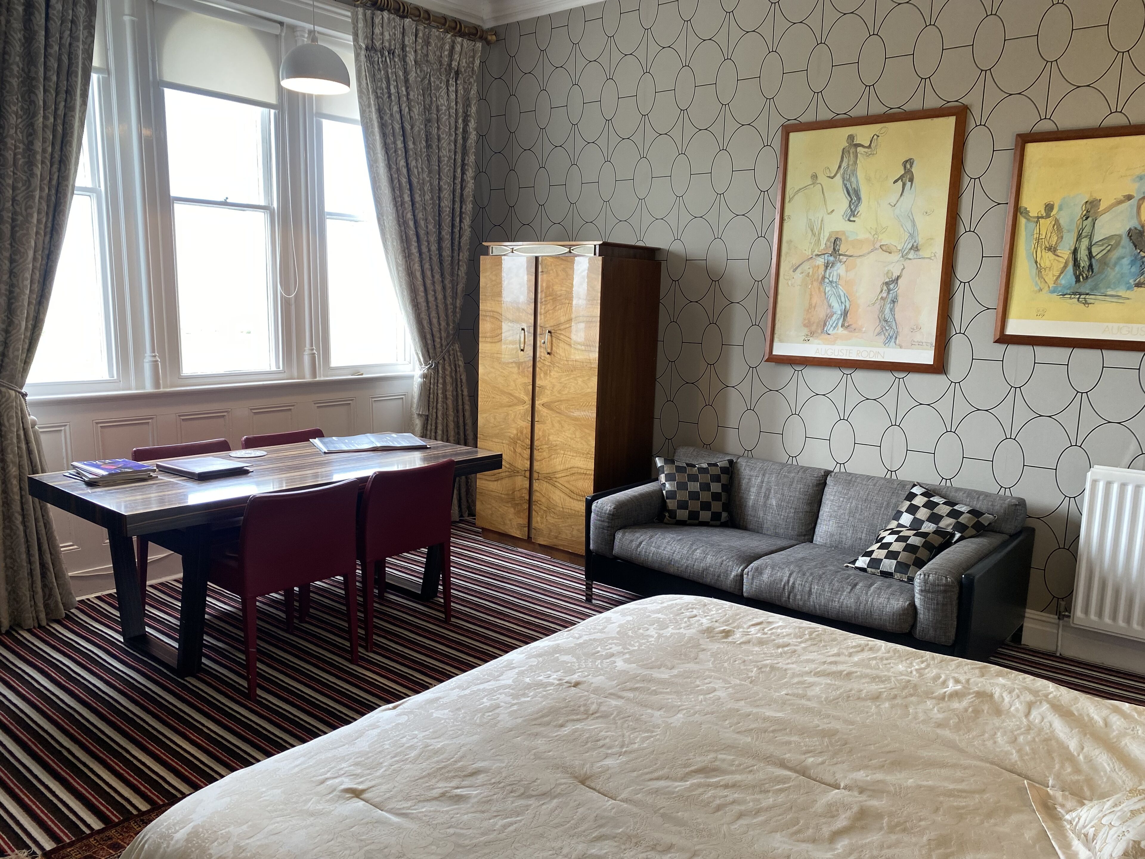 Una habitación de hotel con cama, una mesa de comedor con sillas, un sofá y obras de arte en las paredes.